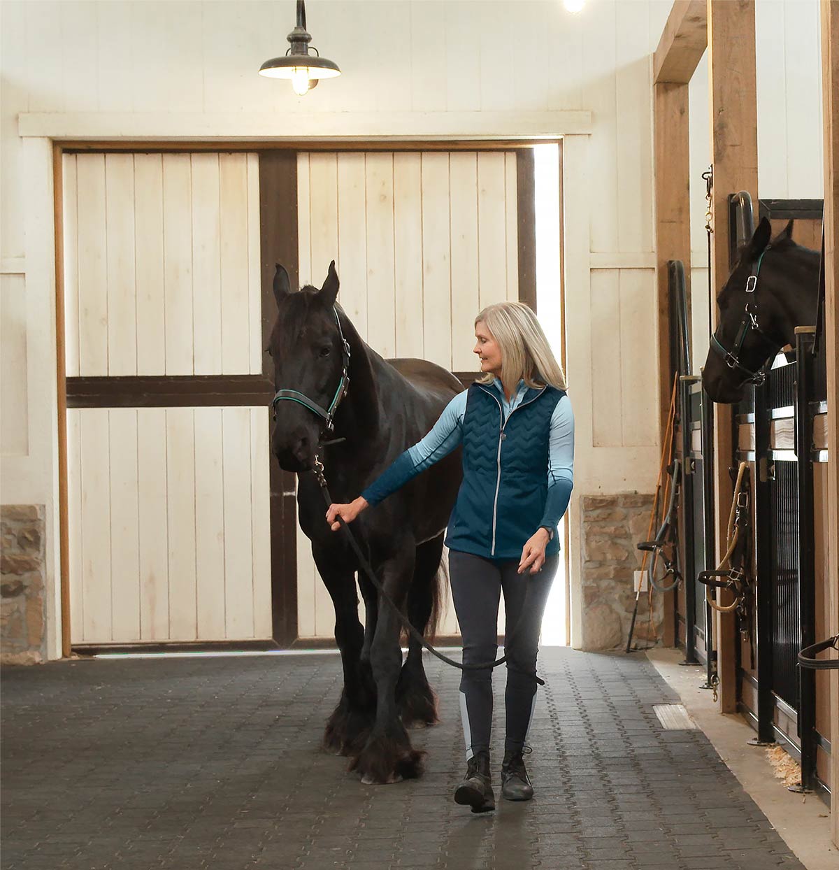 Trainer leading horse into a Classic Equine Equipment stall. Tru-Step® paver flooring in barn interior.