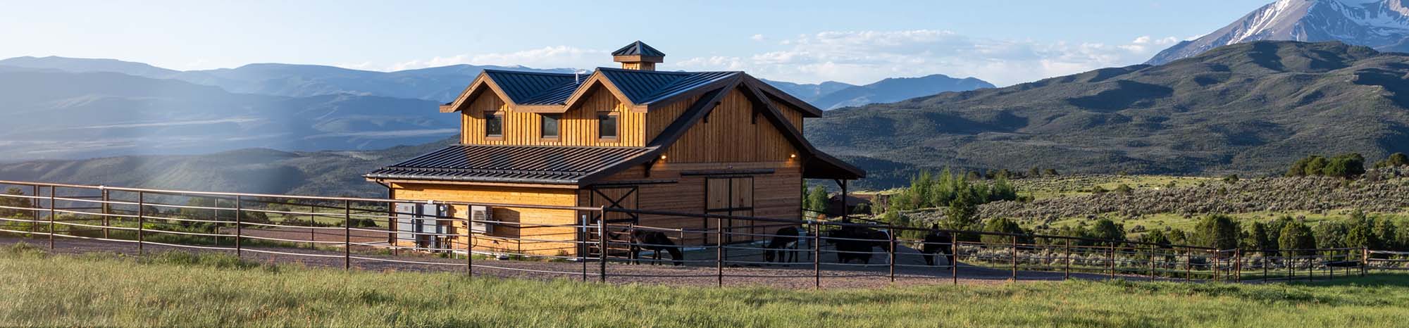 Exterior of horse barn in Colorado. Donkeys in turnout with mountain terrain in the background.