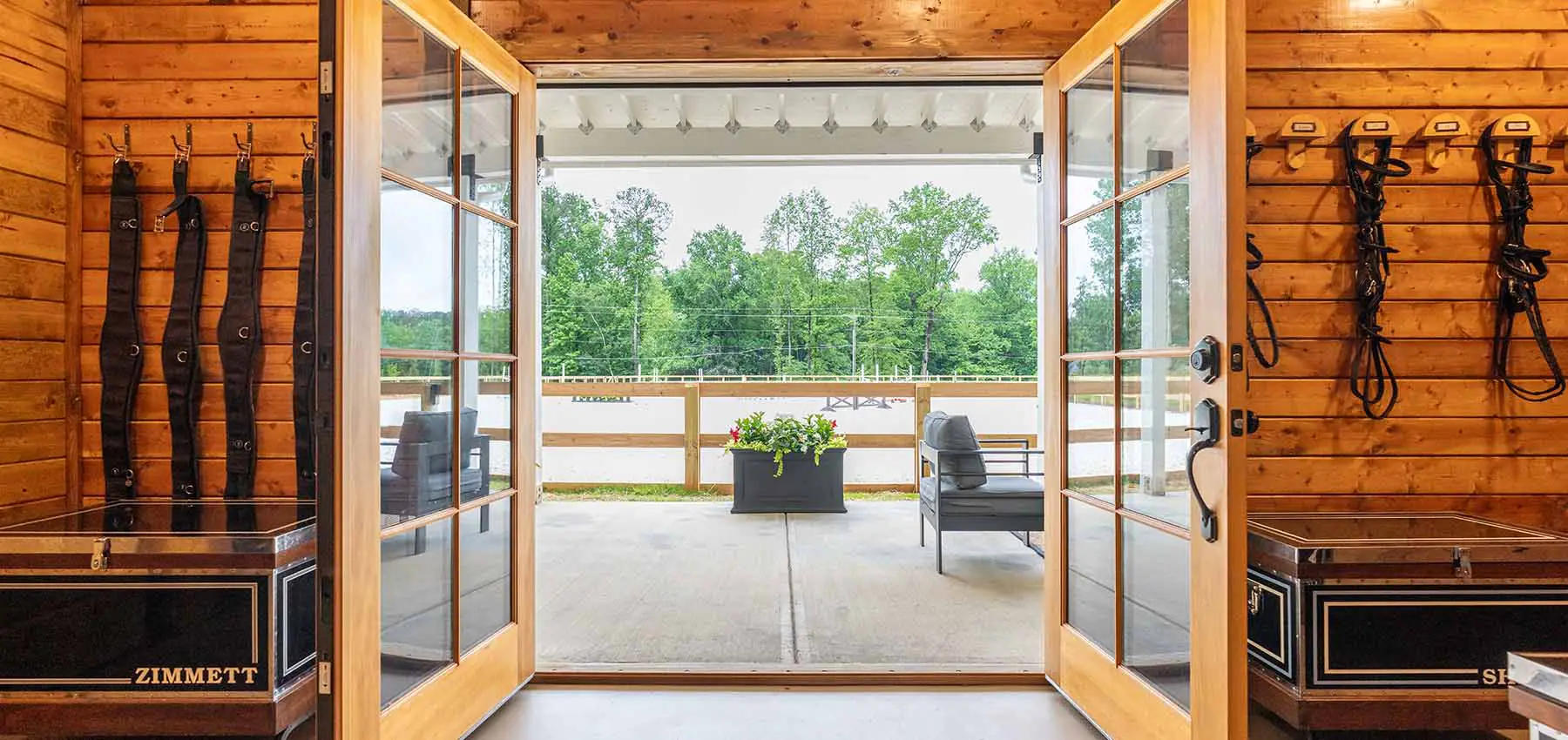 Tack room double doors with mullion design. Leading to outdoor patio entry with view of the riding arena.