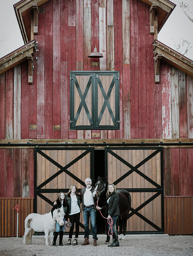 Exterior of barn end doors and loft doors. Family with horses in front of barn.